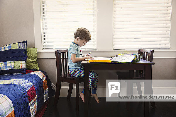 Junge studiert auf Tisch im Schlafzimmer gegen Fenster
