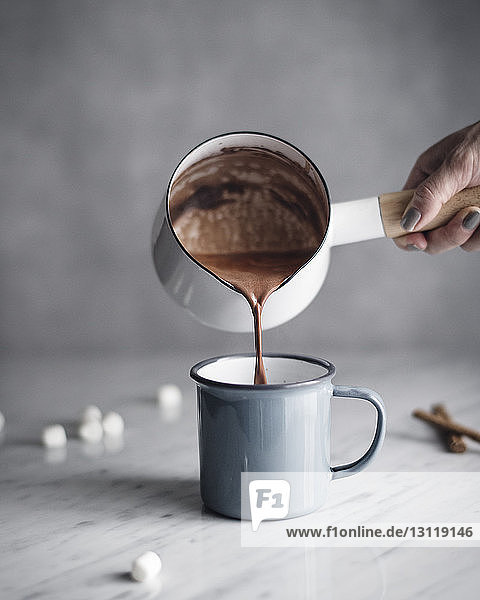 Cropped image of woman pouring hot chocolate in mug on table