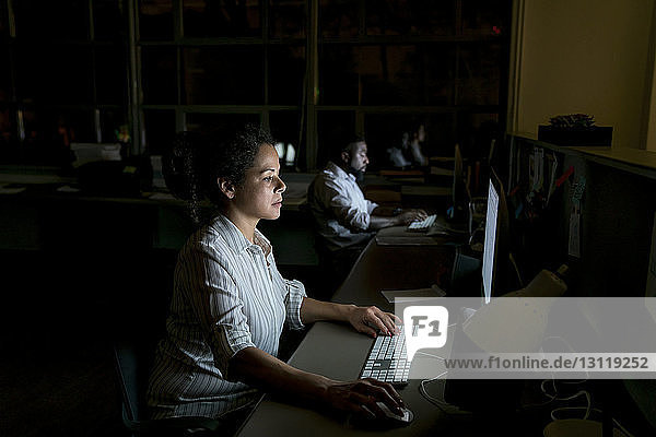 Kollegen arbeiten an Desktop-Computern am Schreibtisch in einem dunklen Büro