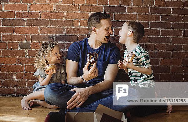 Father with children eating donuts while sitting on floor at home