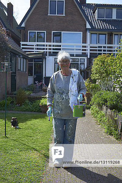 Porträt einer älteren Frau mit Farbdose und Pinsel vor dem Haus stehend