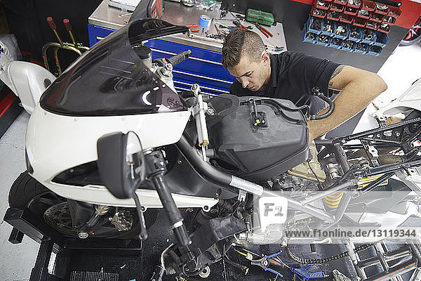 Schrägaufnahme eines Arbeiters  der ein Motorrad in der Werkstatt repariert