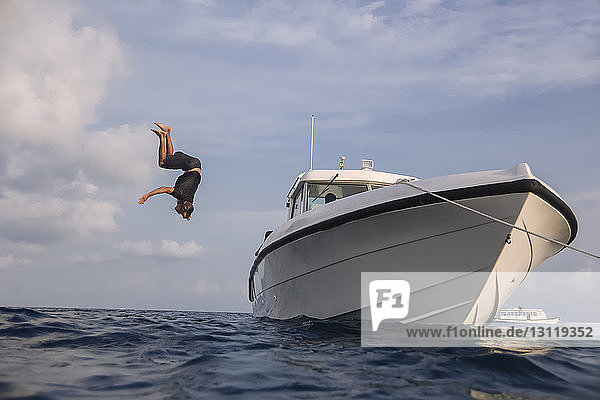 Tiefwinkelaufnahme eines Mannes  der von einer Yacht ins Meer taucht  vor bewölktem Himmel auf den Malediven