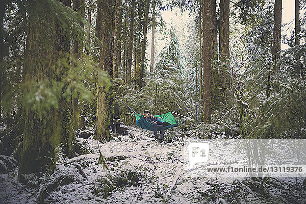 Couple resting in hammock amidst forest at Lynn Canyon Park during winter