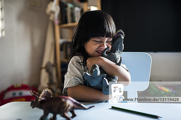 Verspielter Junge umarmt Spielzeug bei Tisch zu Hause