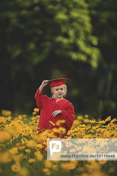 Smiling girl wearing graduation gown standing amidst yellow flowers on field