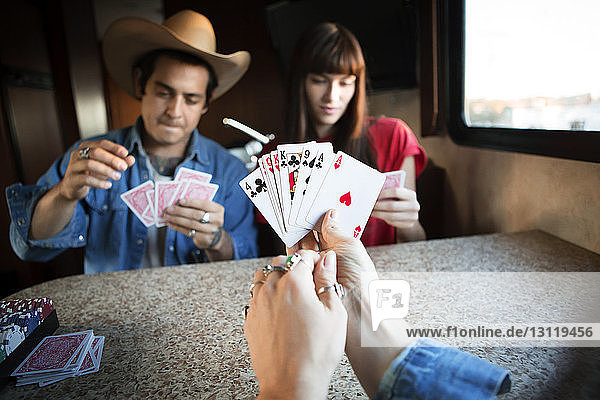 Nahaufnahme einer Frau  die Karten hält  während sie mit Freunden im Wohnmobil spielt