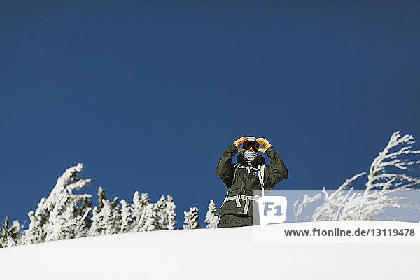 Low angle view of man standing on snow covered mountain against clear blue sky during sunny day