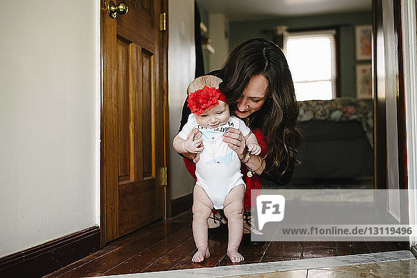 Lächelnde Mutter hilft Tochter zu Hause beim Gehen auf dem Boden