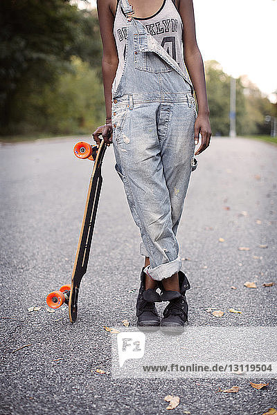 Niedriger Teil einer Frau  die ein Skateboard hält und auf der Straße steht
