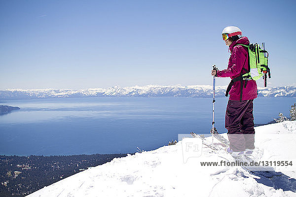 Side view of female skier standing on snowcapped mountain against clear sky