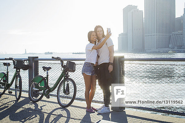 Glückliches Paar  das sich am sonnigen Tag beim Stehen am Fahrrad über das Mobiltelefon selbstständig macht