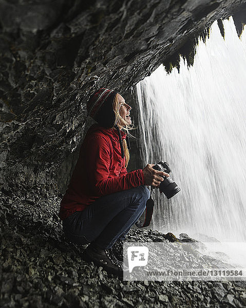 Fröhliche Wanderin schaut auf Wasserfall  während sie die Kamera hält
