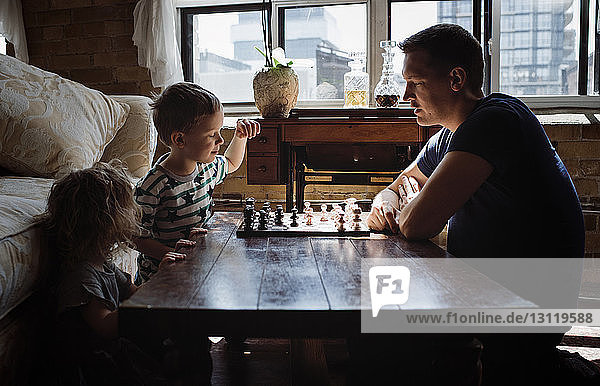 Vater spielt zu Hause mit Kindern am Tisch Schach