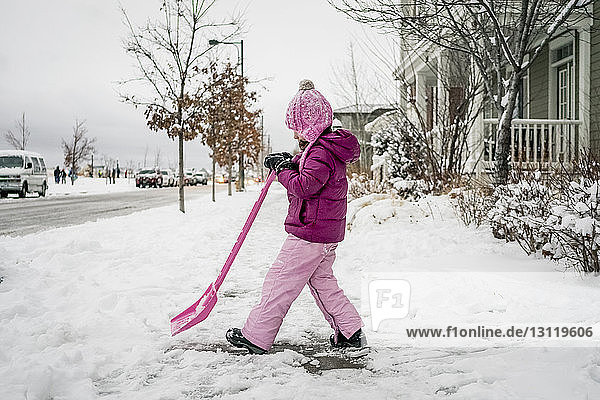 Side view of girl removing snow with shovel on road against sky