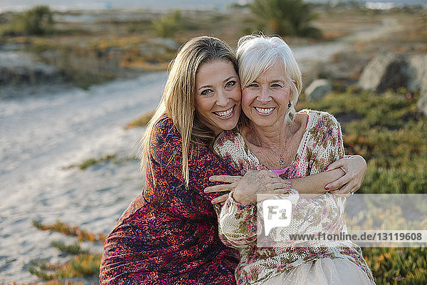 Portrait of happy mother and daughter sitting at beach