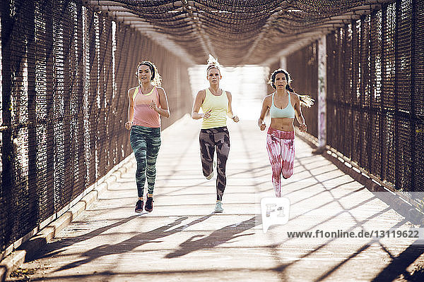 Athletinnen in voller Länge auf einer überdachten Brücke an einem sonnigen Tag joggen
