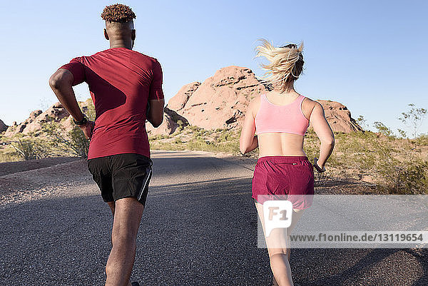 Rear view of hikers running on road against clear sky