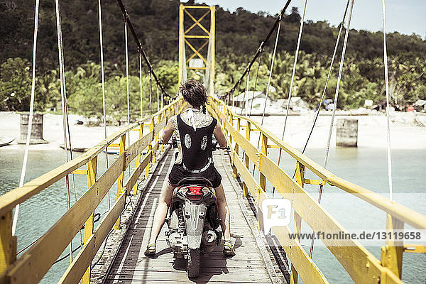Rear view of woman riding scooter on bridge