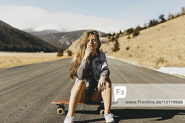 Porträt einer selbstbewussten jungen Frau  die an einem sonnigen Tag auf einem Skateboard sitzt