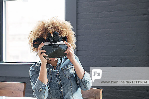 Geschäftsfrau benutzt Virtual-Reality-Simulator  während sie im Büro am Tisch sitzt