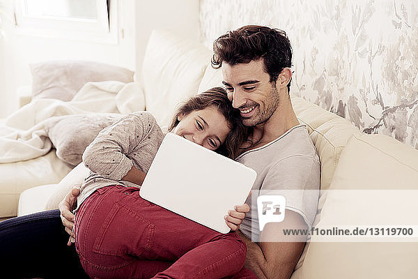 Glücklicher Vater und Tochter lesen digitales Tablett  während sie sich auf dem Sofa ausruhen