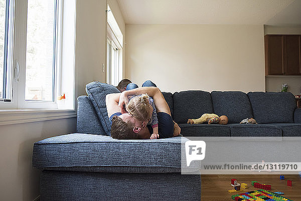Glücklicher Vater spielt zu Hause mit Kindern auf dem Sofa