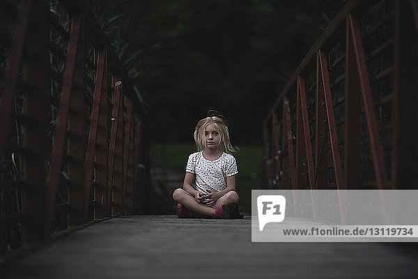 Thoughtful girl sitting on footbridge at park