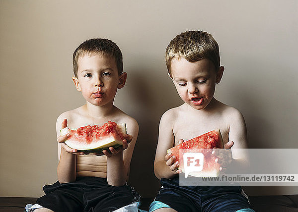 Portrait of boy eating watermelon with brother at home