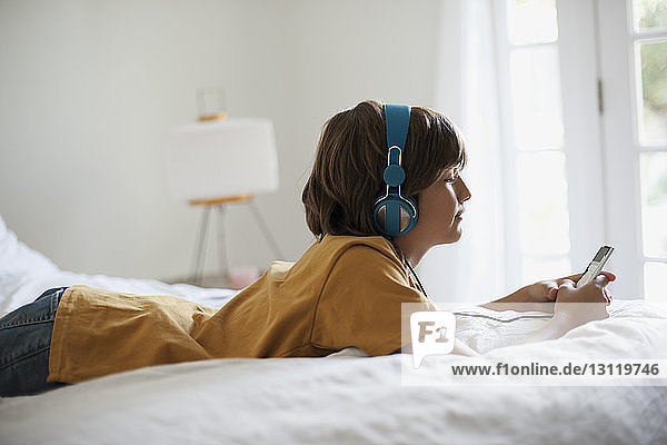 Side view of boy listening music while lying on bed at home