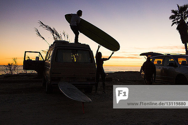 Scherenschnitt eines Mannes  der einer Frau ein Surfbrett reicht  während er auf einem Kleinbus am Strand des Bundesstaates San Onofre steht