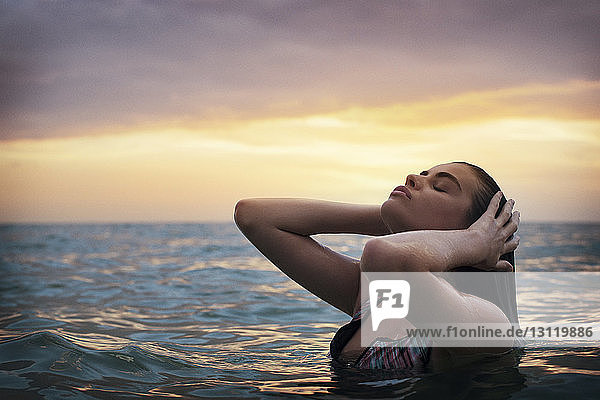 Nahaufnahme einer jungen Frau  die sich bei Sonnenuntergang am Meer gegen den Himmel genießt