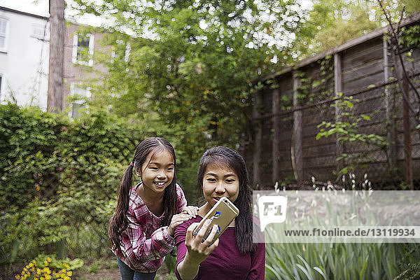 Fröhliche Schwestern  die in der Stadt an Pflanzen sitzend Selbsthilfe am Telefon betreiben