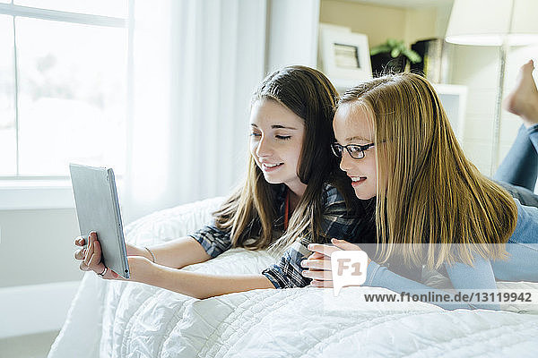 Schwestern benutzen Tablet-Computer  während sie auf dem Bett liegen