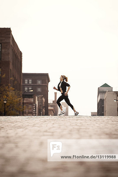 Side view of woman jogging on city street against clear sky