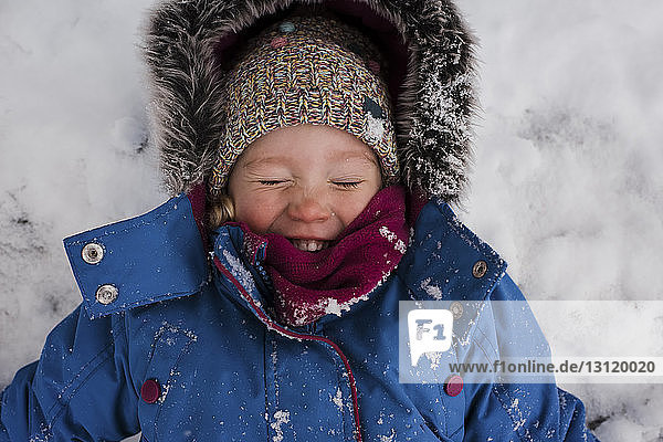 High angle view of smiling girl with eyes closed lying on snow covered field