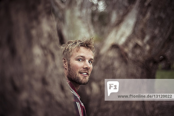 Lächelnder selbstbewusster Mann steht am Baum im Wald