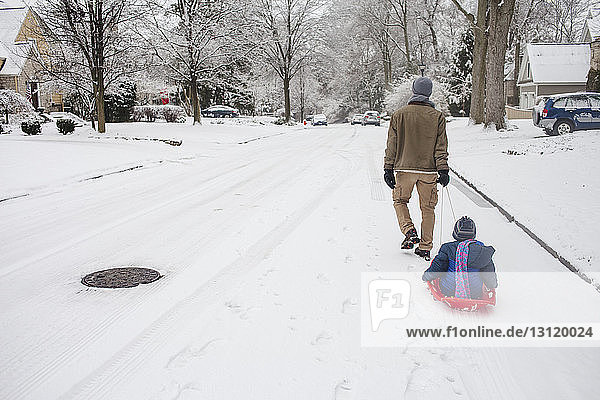 Rear view of father sledding daughter on snow covered road