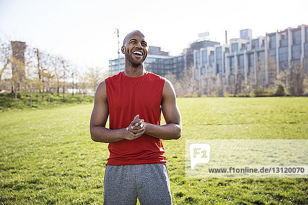 Cheerful male athlete standing on grassy field in city
