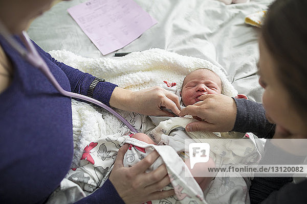 Hochwinkelansicht einer Hebamme  die ein neugeborenes Mädchen von einer Frau zu Hause im Bett untersucht