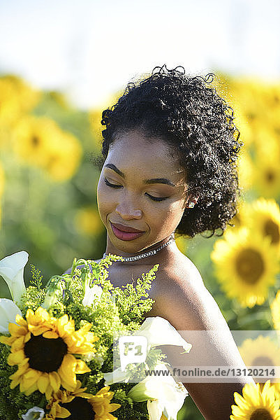 Nahaufnahme einer Braut  die einen Brautstrauss hält  während sie auf dem Bauernhof gegen Sonnenblumen steht