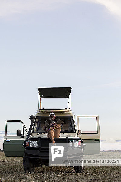 Mann in voller Länge auf Fahrzeug im Serengeti-Nationalpark gegen den Himmel sitzend