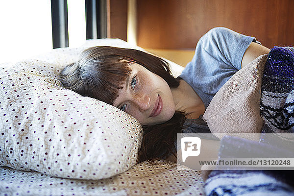 Portrait of woman lying on bed in camper van