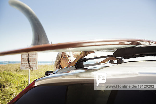 Reife Frau bindet Surfbrett auf Autodach am Delray-Strand vor klarem blauen Himmel