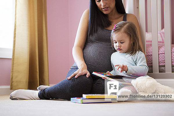 Nahaufnahme einer schwangeren Frau mit Tochter beim Betrachten eines Buches