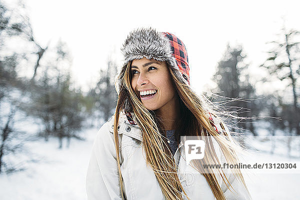 Nahaufnahme einer fröhlichen Frau mit Pelzmütze  die auf einem schneebedeckten Feld steht