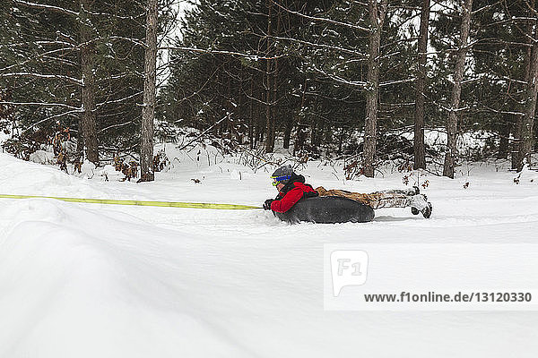Teenage boy being towed with inflatable ring on snow covered field in forest