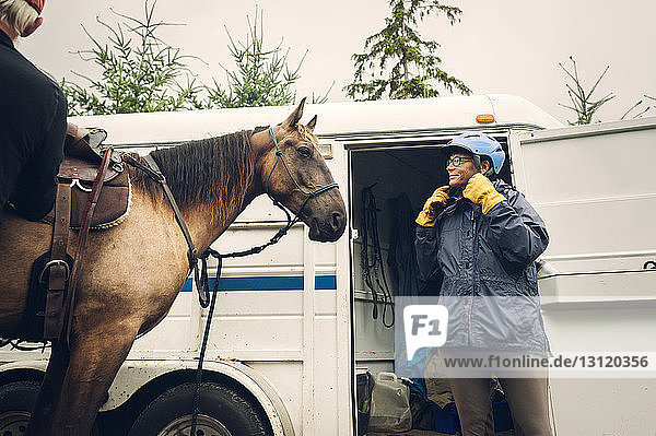 Ärztin mit Helm beim Stehen mit Pferd gegen Krankenwagen