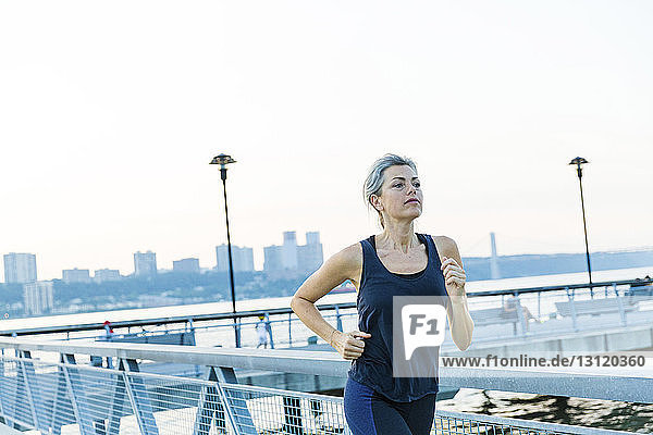 Woman jogging while exercising on bridge against clear sky