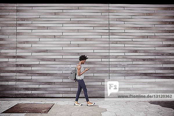 Side view of woman using smart phone while walking against wall